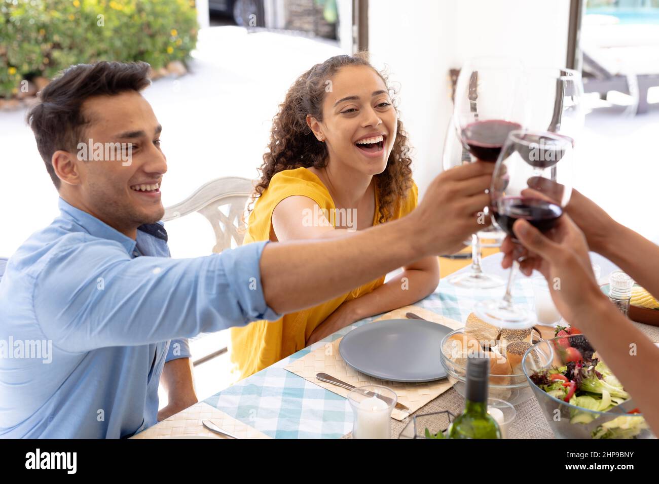 Uomini e donne allegri che tostano i wineglasses mentre si siedono insieme al tavolo da pranzo Foto Stock