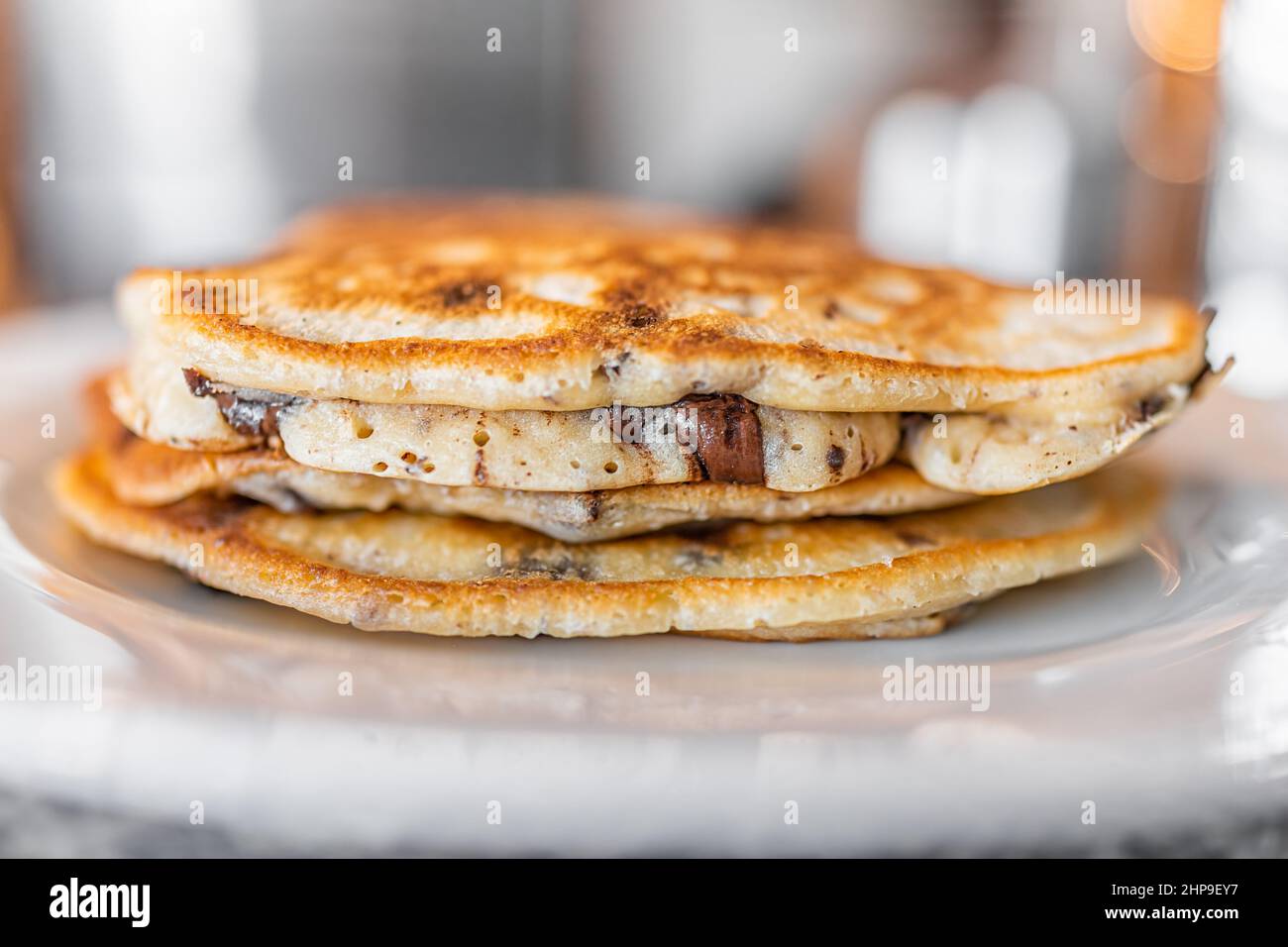 Macro primo piano vista laterale di una pila di pancake al burro con scaglie di cioccolato fondente sul piatto come dessert tradizionale per il brunch della colazione Foto Stock