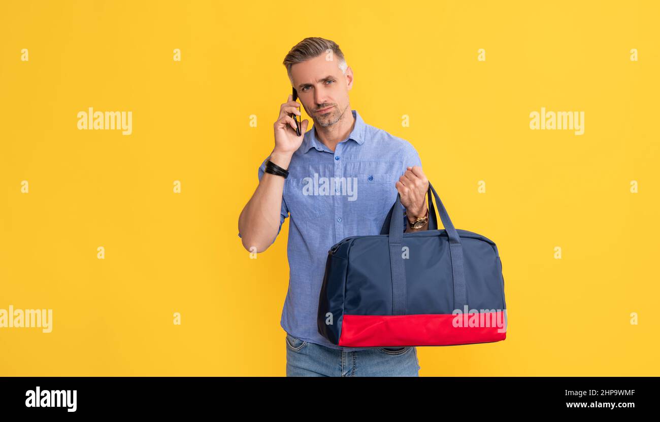 uomo d'affari parla su smartphone con borsa da viaggio. uomo ha conversazione tenere borsa sportiva. Foto Stock