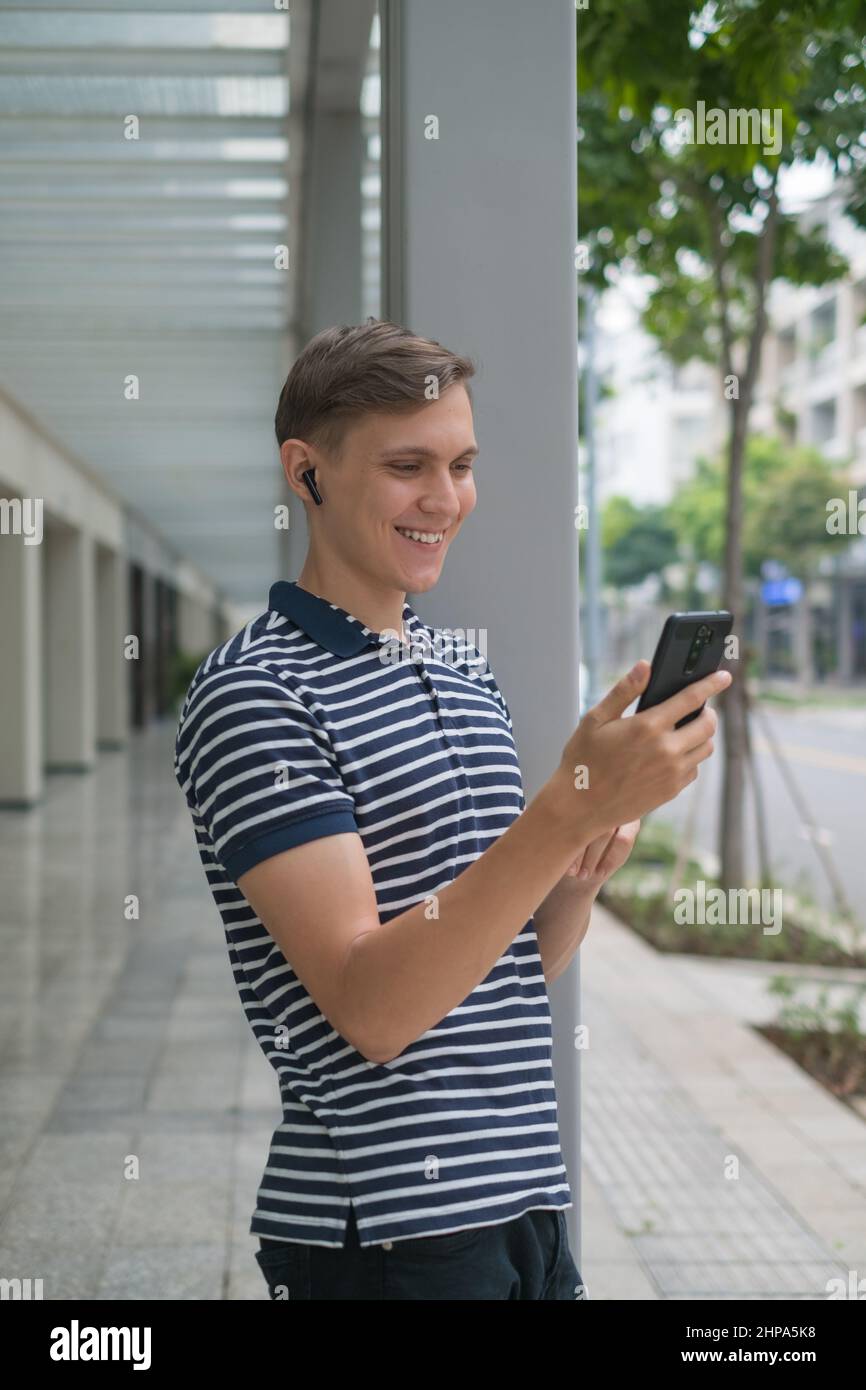 Felice giovane uomo caucasico si trova sulla strada e fa videochiamata al telefono e sorridente. Utilizzando lo smartphone. Foto di alta qualità Foto Stock
