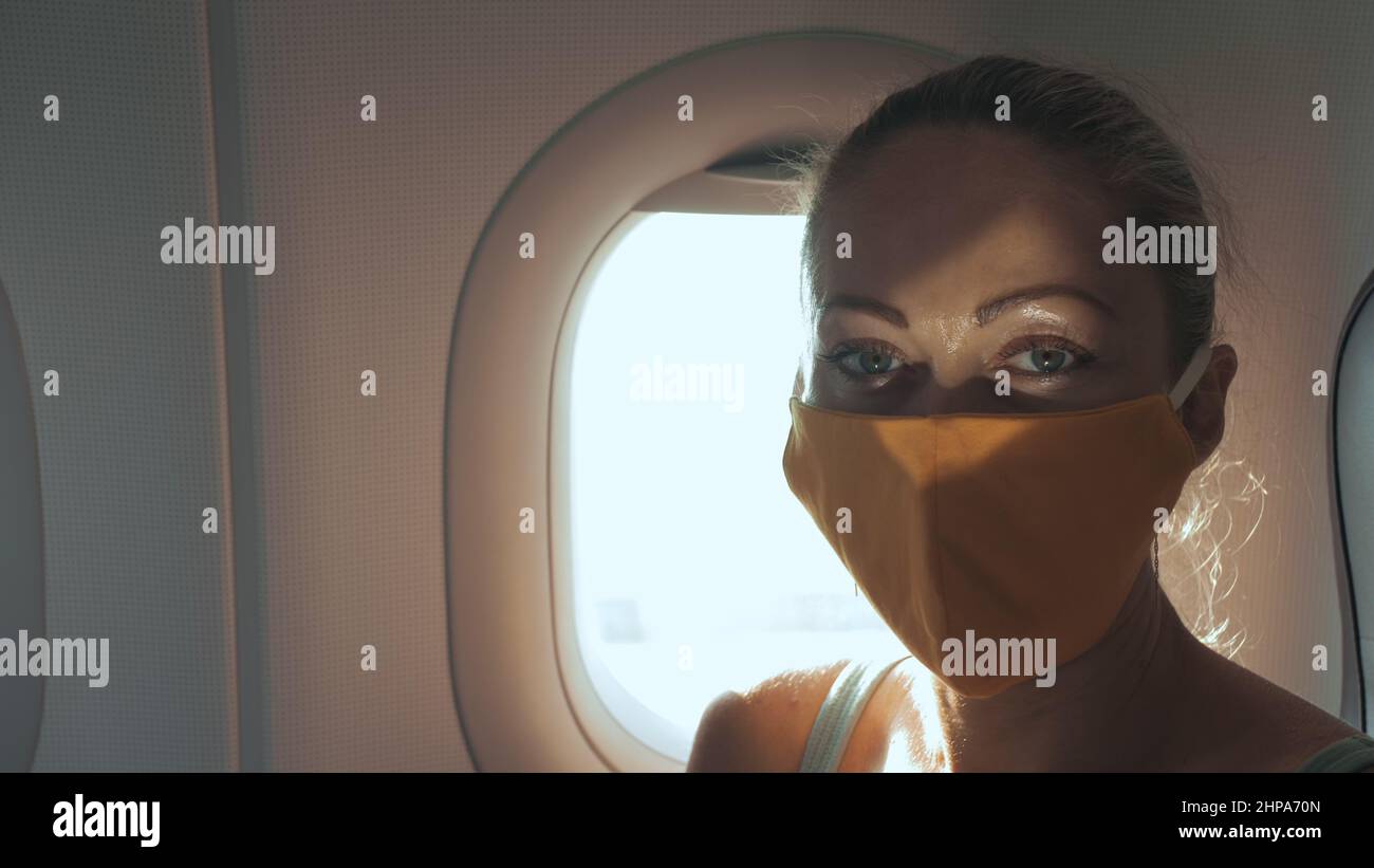 Donna viaggio caucasico in aereo con indossare maschera medica protettiva. Ragazza turistica in aereo con respiratore di protezione. Concetto di protezione antivirus coron Foto Stock