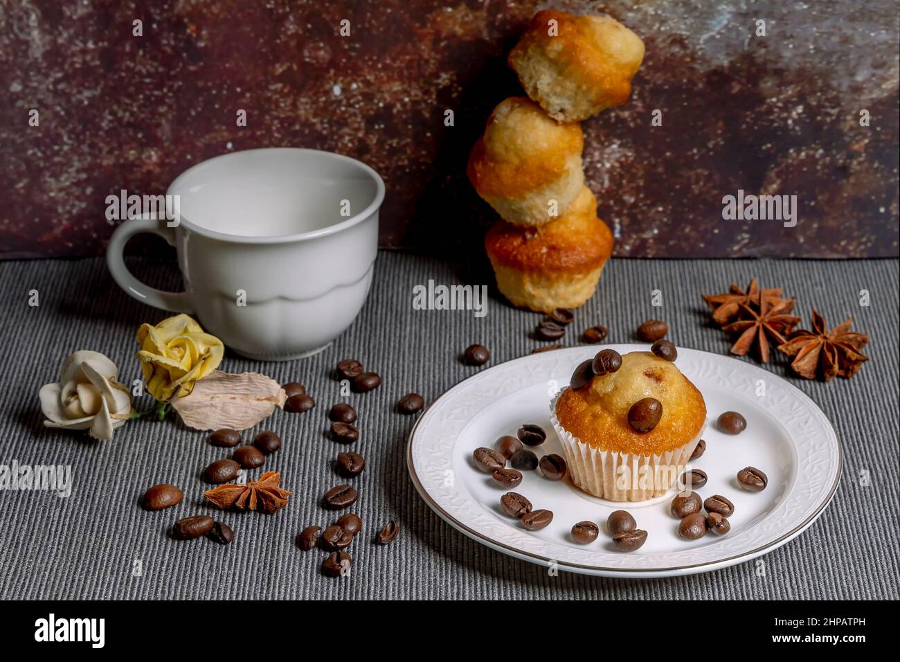 Muffin con chicchi di caffè, anice stellato e fiori finti, accanto a una tazza di caffè espresso Foto Stock