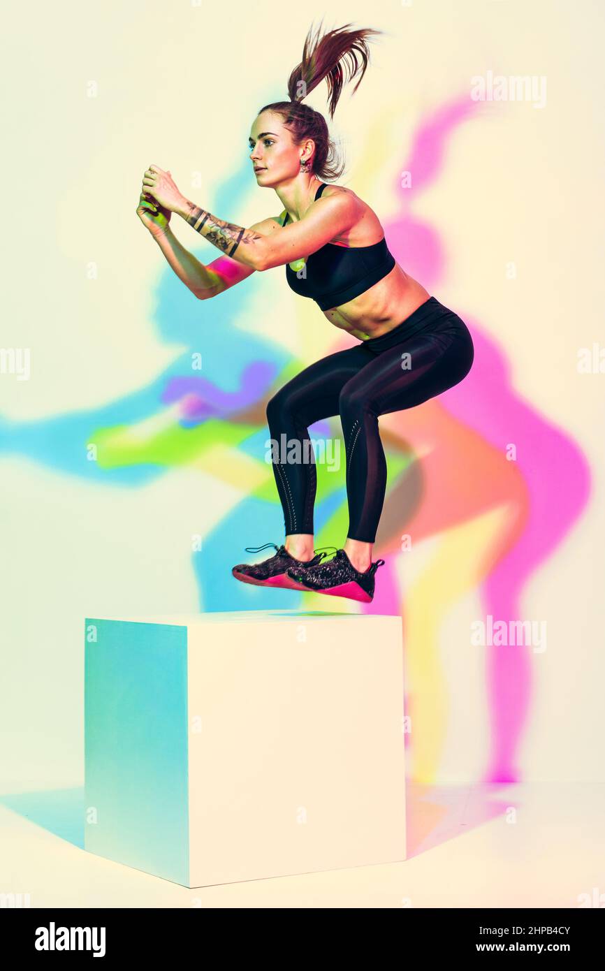 Donna sportiva che fa box salto esercizio. Foto di donna atletica in nero sportswear su sfondo bianco con effetto rgb colori ombre. Resistenza e. Foto Stock