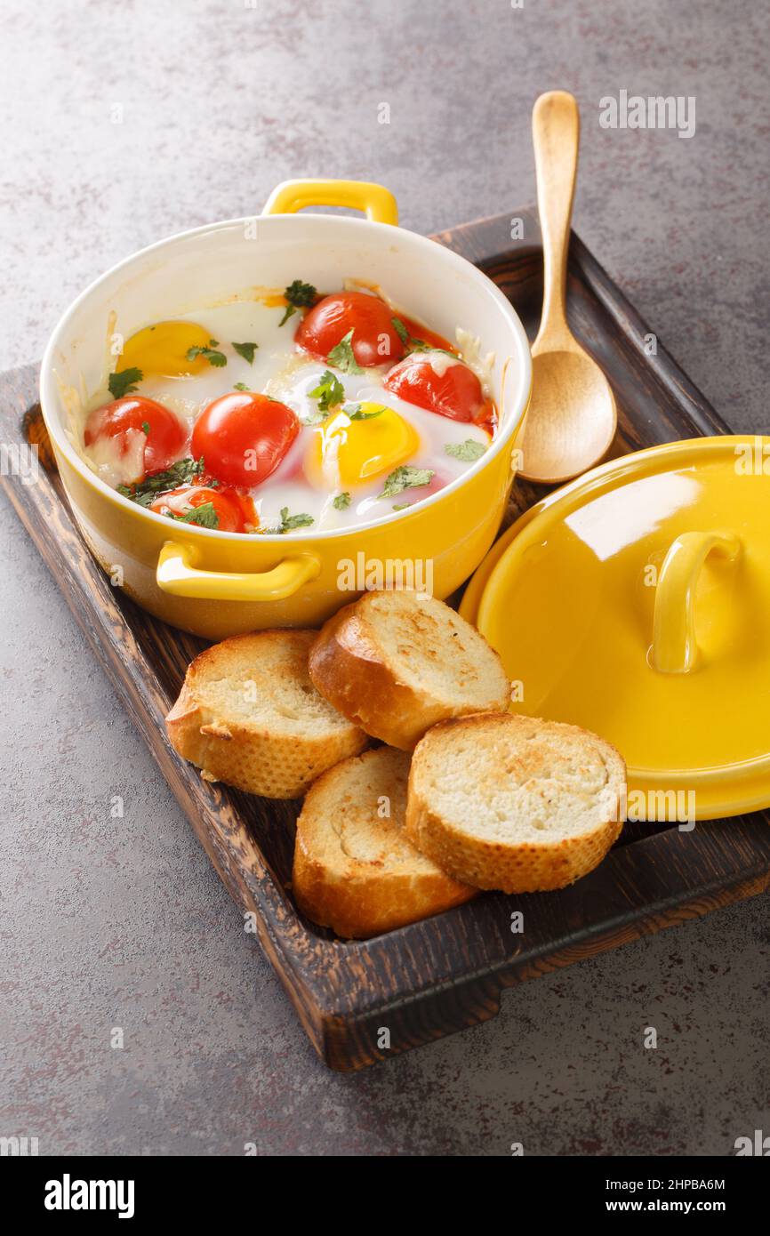 Oeufs cocotte è un modo francese di cuocere le uova in un bagno d'acqua nel forno vicino nel vassoio di legno sul tavolo. Verticale Foto Stock