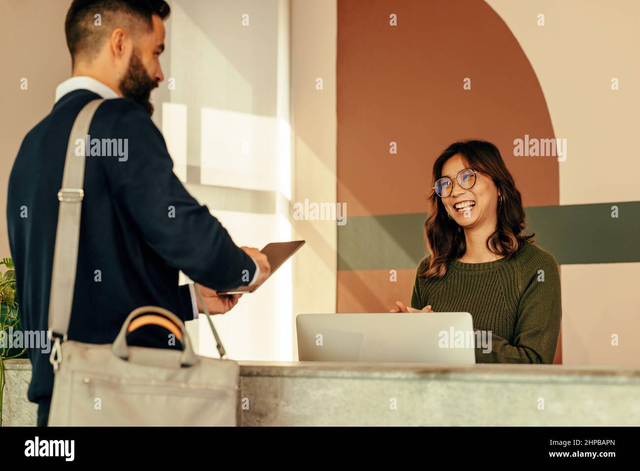 Una buona receptionist che assiste un uomo con l'accesso ad un ufficio. L'addetto alla reception è cordiale e ha preso la firma di un uomo d'affari su un tablet digitale. Giovane vom Foto Stock