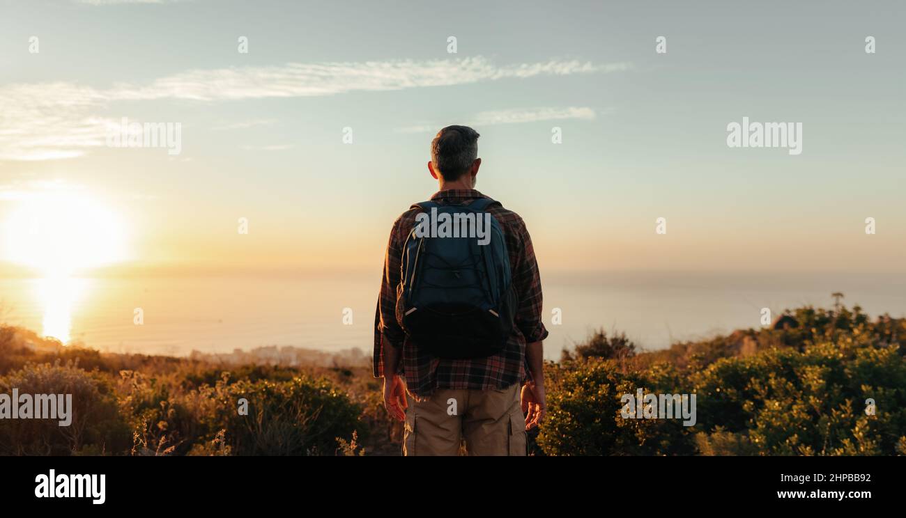 Vista posteriore di uno zaino in spalla che guarda la vista panoramica su una collina. Escursionista maschile irriconoscibile in piedi da solo su una collina costiera. Ma maturo avventuroso Foto Stock