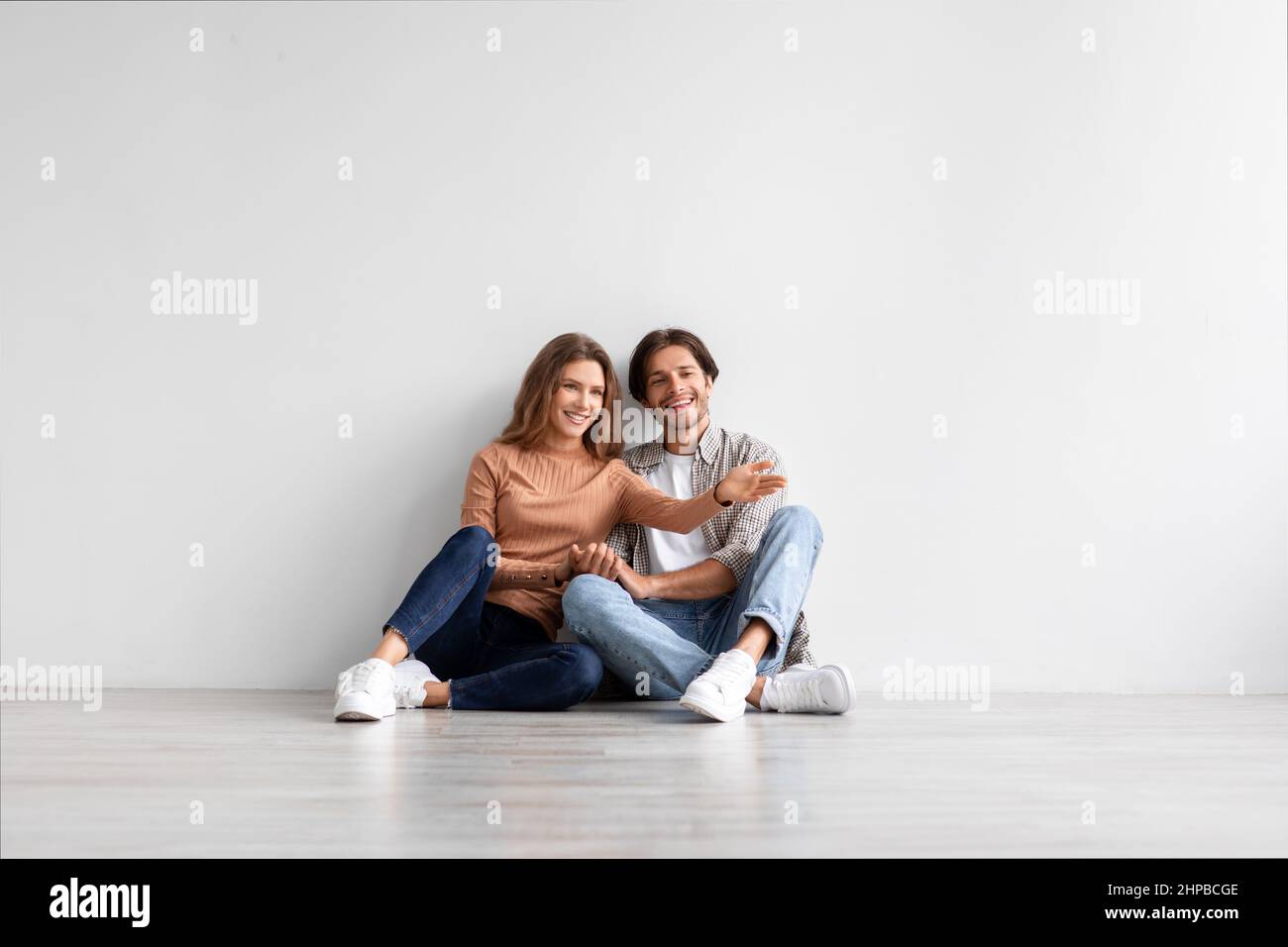 Sorridente uomo caucasico millenario e signora celebrare l'acquisto di un proprio appartamento, la progettazione di interni in camera vuota Foto Stock