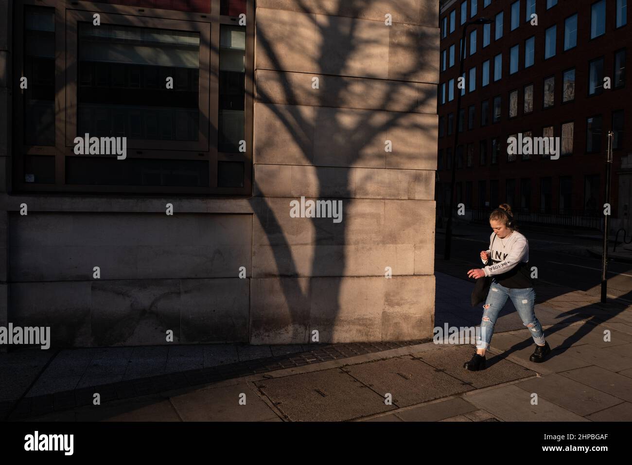 Donna fa la sua strada lungo una strada londinese in bella luce calda tramonto. Sulla parete dell'edificio si può vedere l'ombra di un albero. Foto Stock