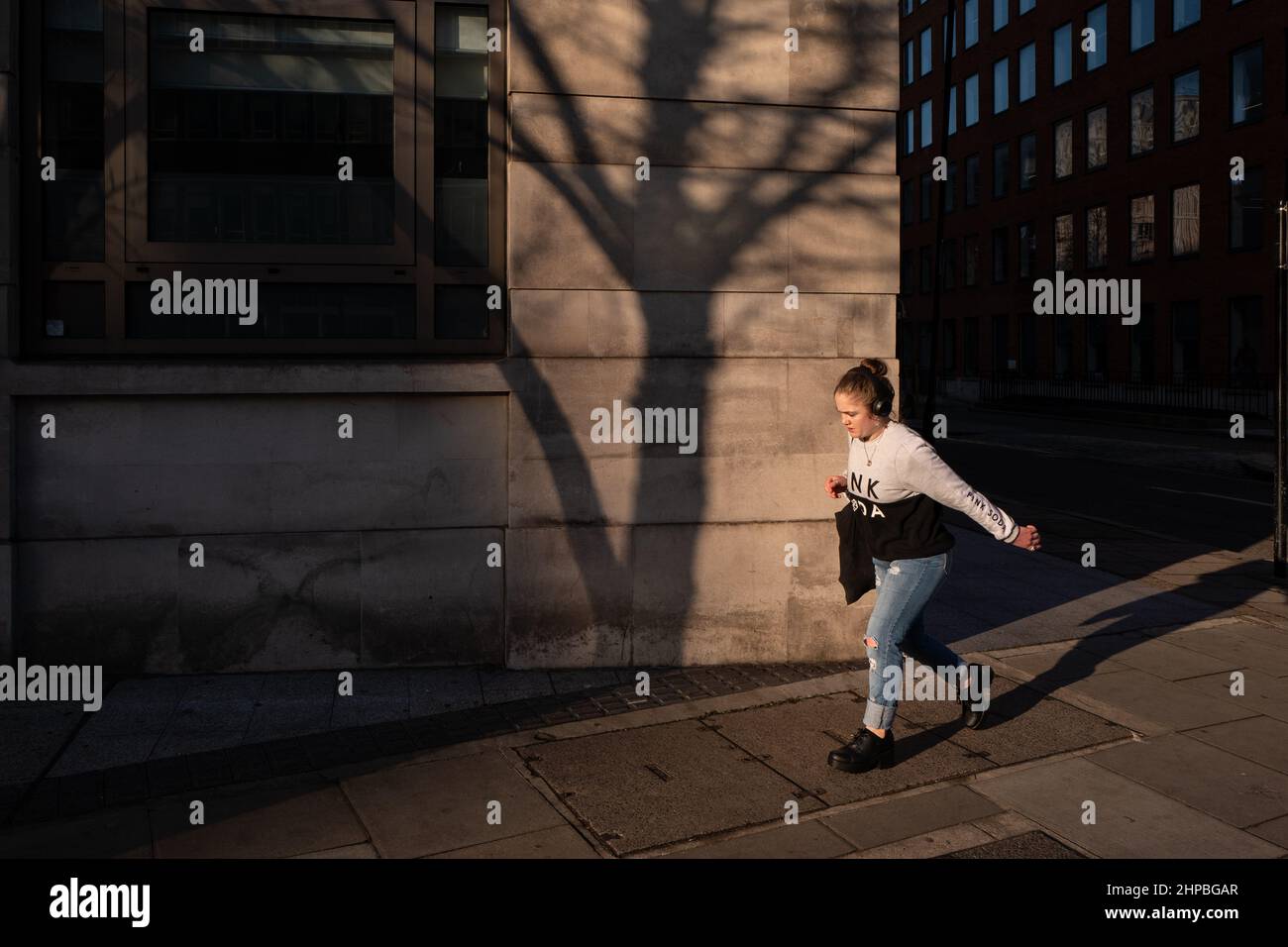 Donna fa la sua strada lungo una strada londinese in bella luce calda tramonto. Sulla parete dell'edificio si può vedere l'ombra di un albero. Foto Stock