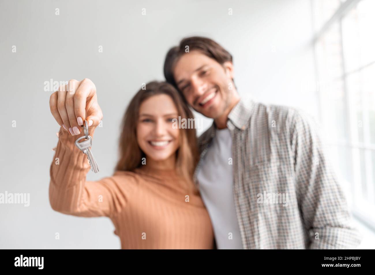 Soddisfatto felice giovane coppia caucasica celebrare l'acquisto proprio appartamento in prestito, mostra le chiavi in camera vuota Foto Stock