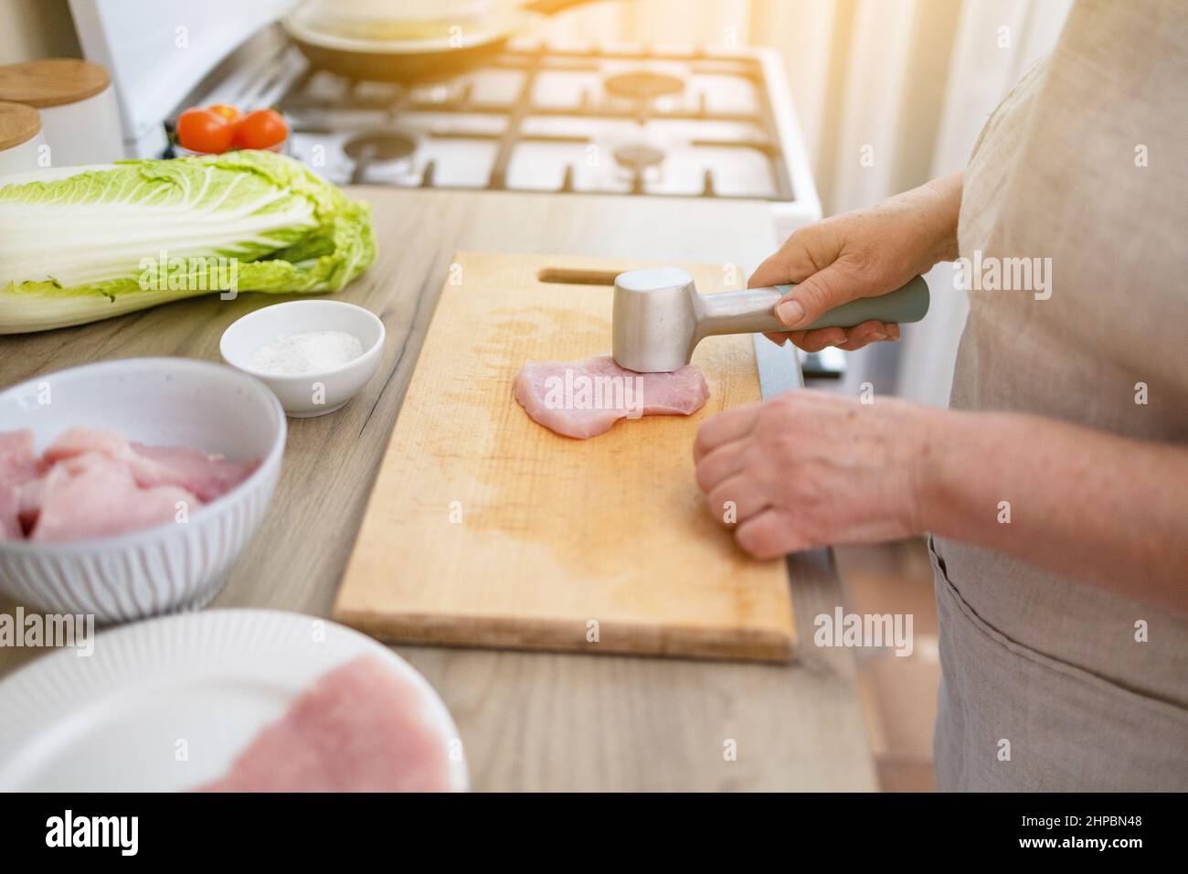 Donna che batte la bistecca di tacchino crudo con il mazzuolo di carne in cucina. Ingredienti per preparare alimenti sani Foto Stock