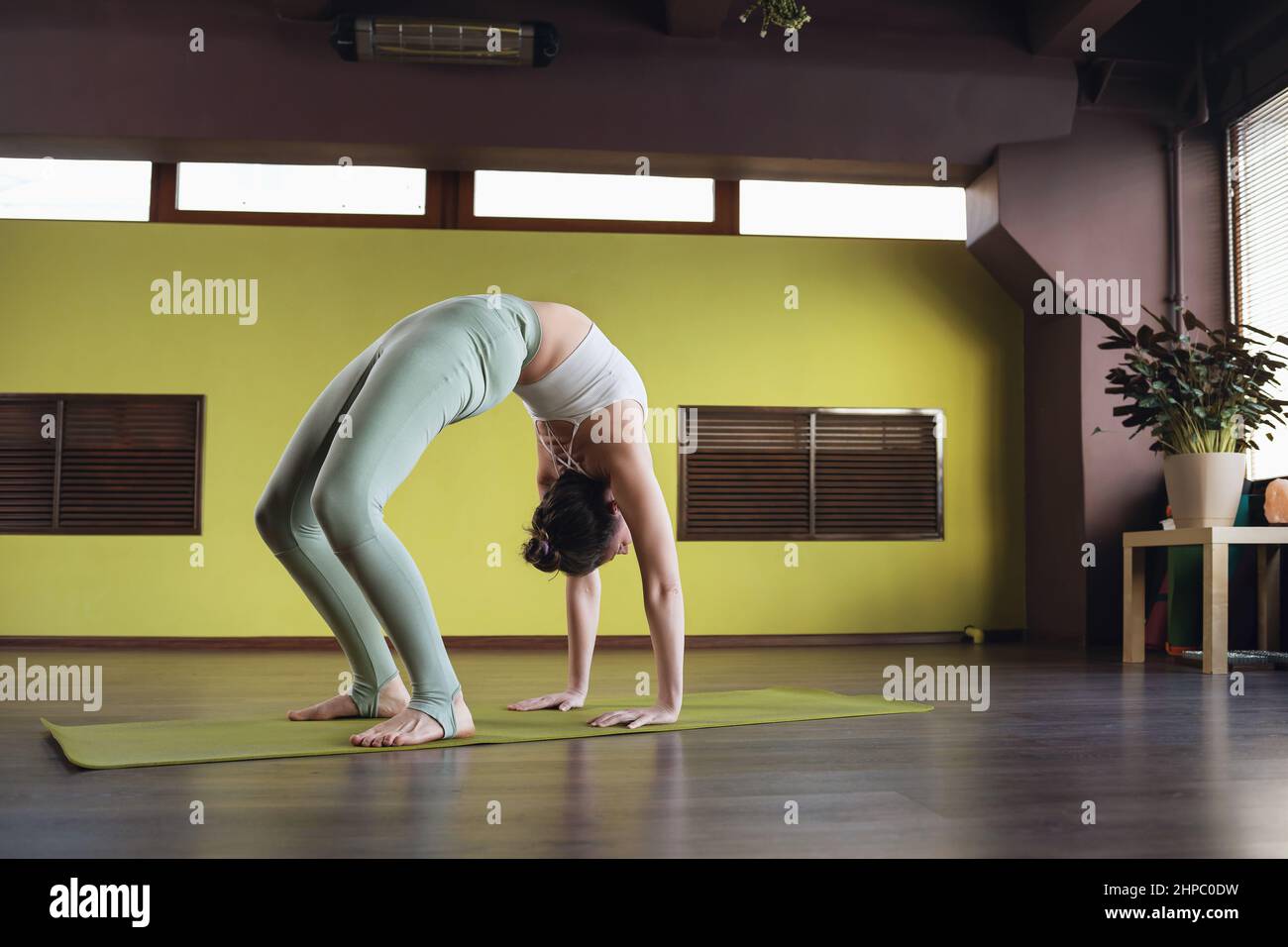 Una donna in abbigliamento sportivo che fa una variante dell'esercizio Setu Bandha Sarvangasana, posa del ponte, in piedi su un tappeto in studio Foto Stock