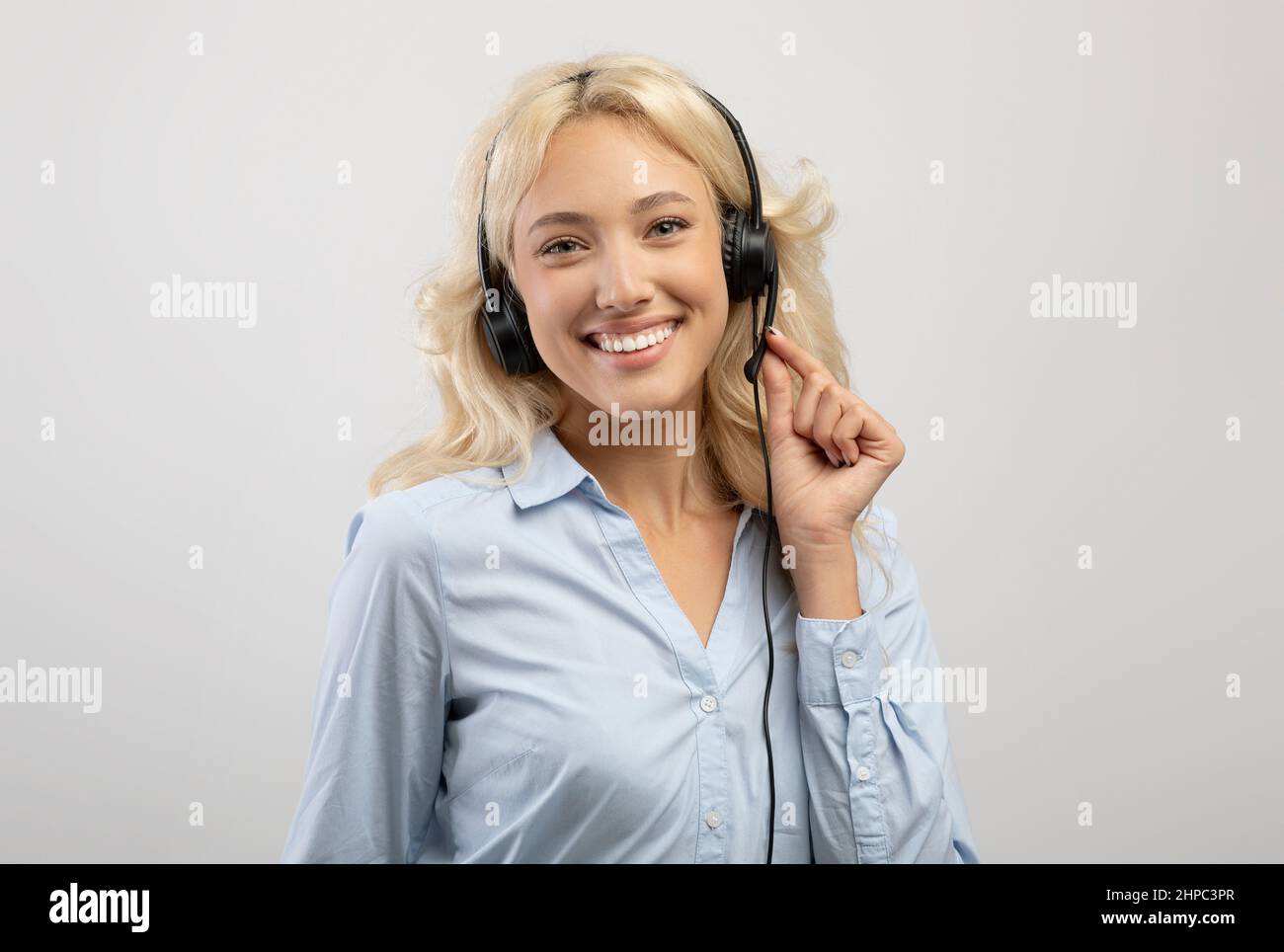 Operatore del servizio clienti. Ritratto di un rappresentante del call center femminile felice in cuffia, posato su sfondo grigio Foto Stock