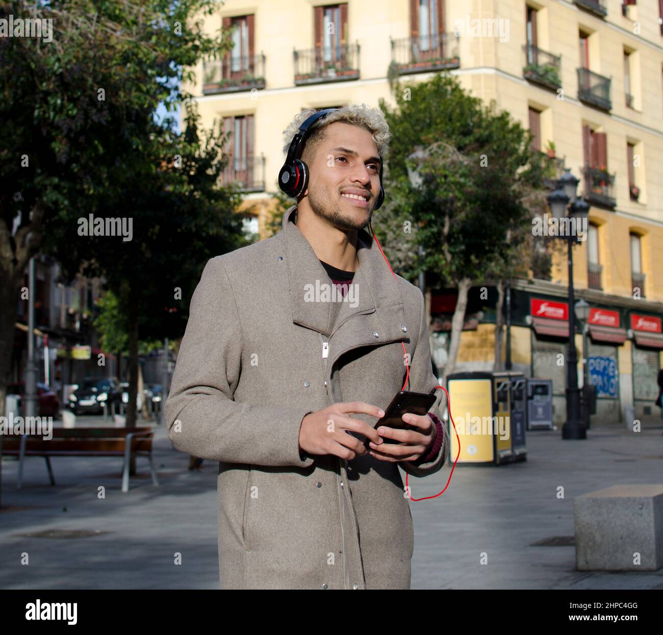 Giovane uomo con cuffie che tengono in mano lo smartphone e che ascolta la musica in città Foto Stock