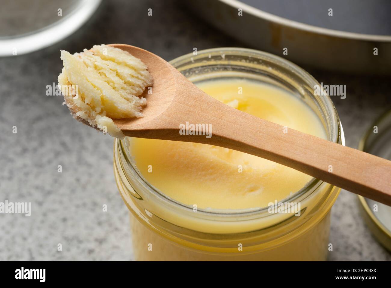 Vaso di vetro e cucchiaio di legno con ghee giallo in primo piano Foto Stock