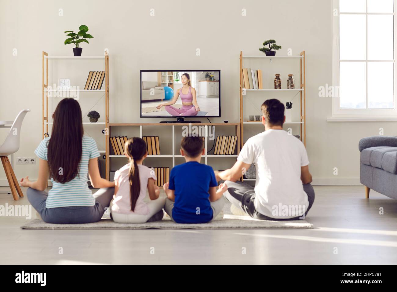 La giovane famiglia con bambini pratica lo yoga e medita insieme a casa davanti allo schermo della TV. Foto Stock