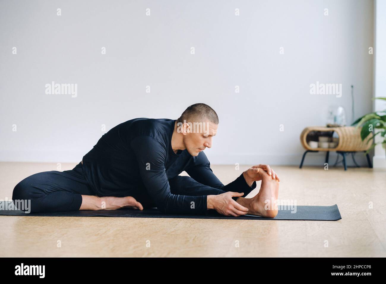 Un uomo di abbigliamento sportivo nero sta facendo yoga, stretching in palestra Foto Stock