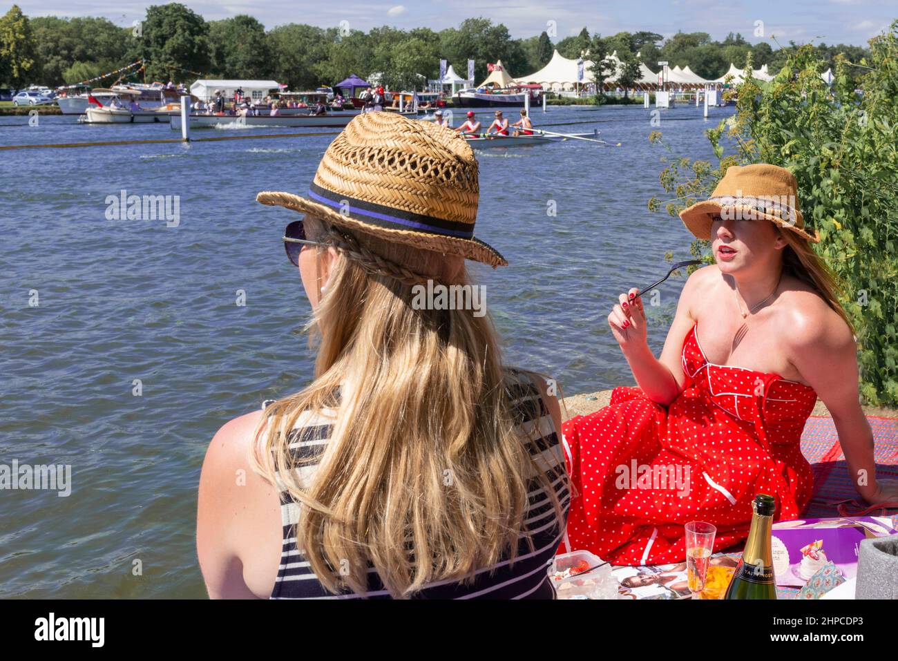 Due ragazze si siedono sulla riva del Tamigi gustando un bicchiere di champagne mentre guardano la Henley Royal Regatta, Henley-on-Thames, Inghilterra, Regno Unito Foto Stock
