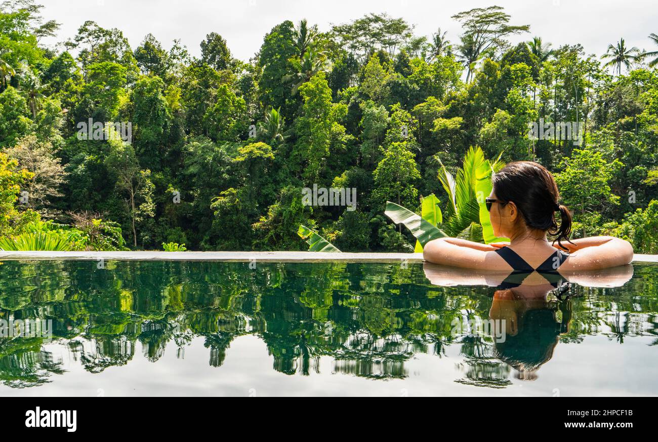 Donna che gode della vista dalla piscina a sfioro del resort di Bali Foto Stock