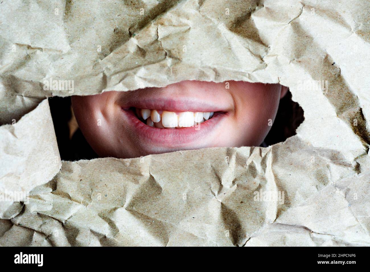 Sorridi con i denti nei fori. Bocca nel foro in uno sfondo di carta sgualcito. Foto Stock