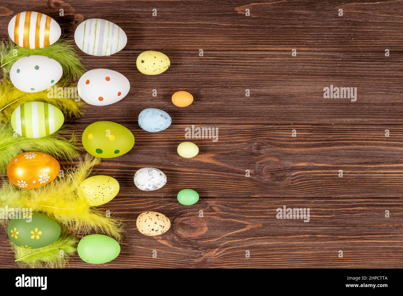 Felice Pasqua concetto. Uova di Pasqua colorate con piume luminose su sfondo di legno scuro. Vista dall'alto. Luogo per l'iscrizione, testo. Base per A. Foto Stock