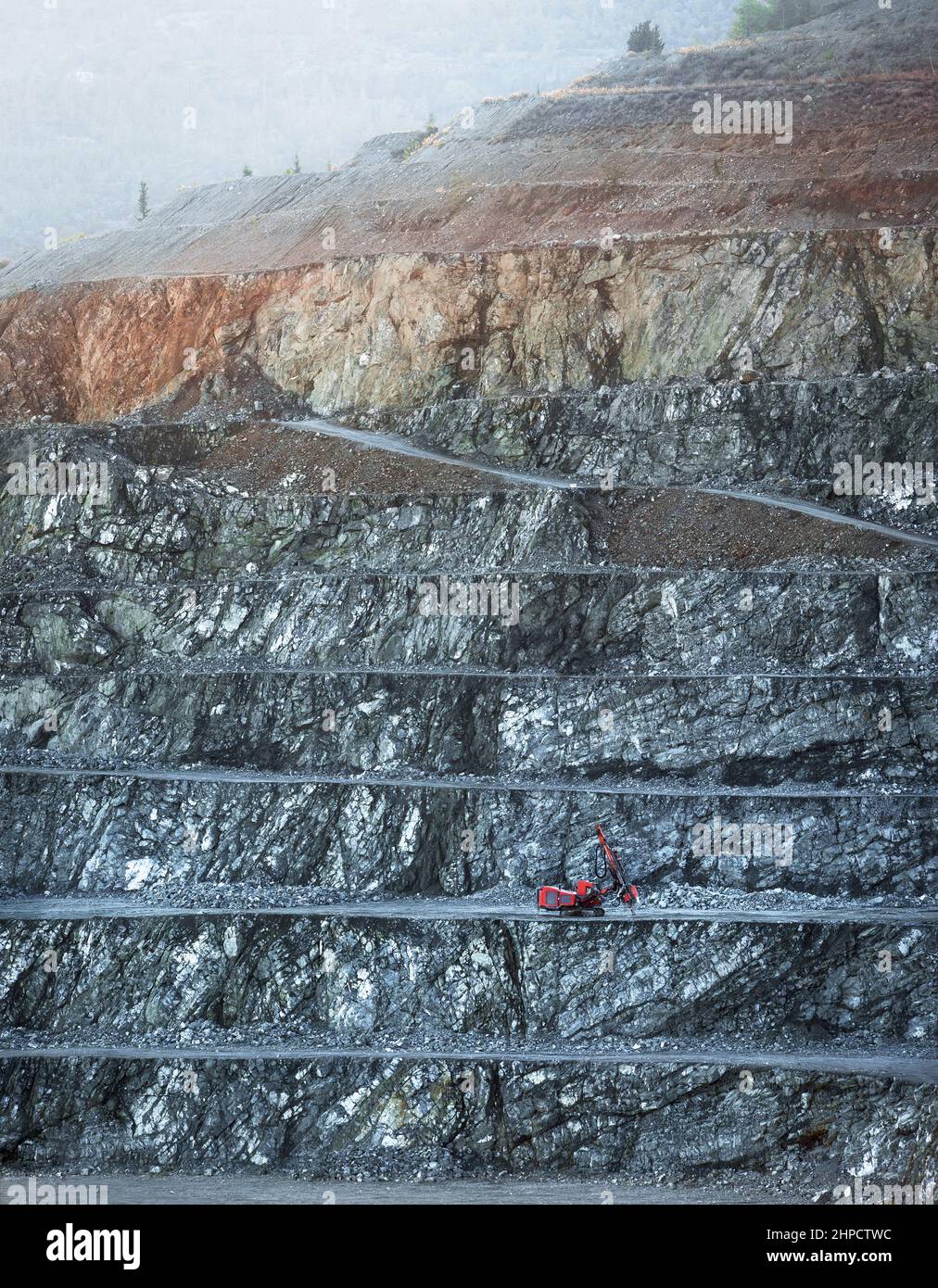 Macchina di perforazione rossa su un banco di cava di diabase in mattinata nebbiosa Foto Stock