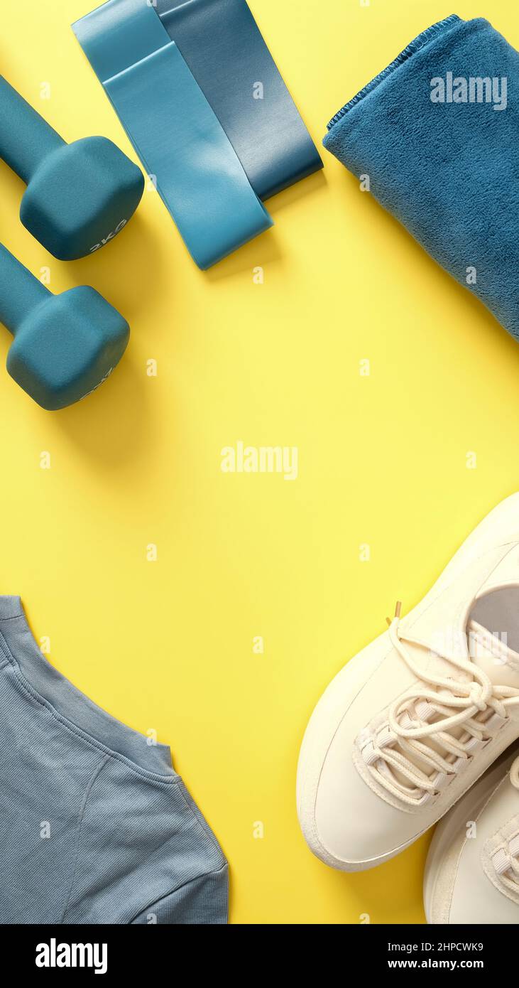 Scarpe sportive, manubri, abbigliamento sportivo, nastro fitness, asciugamano su sfondo giallo vista dall'alto. Fitness, palestra, accessori per l'allenamento Foto Stock