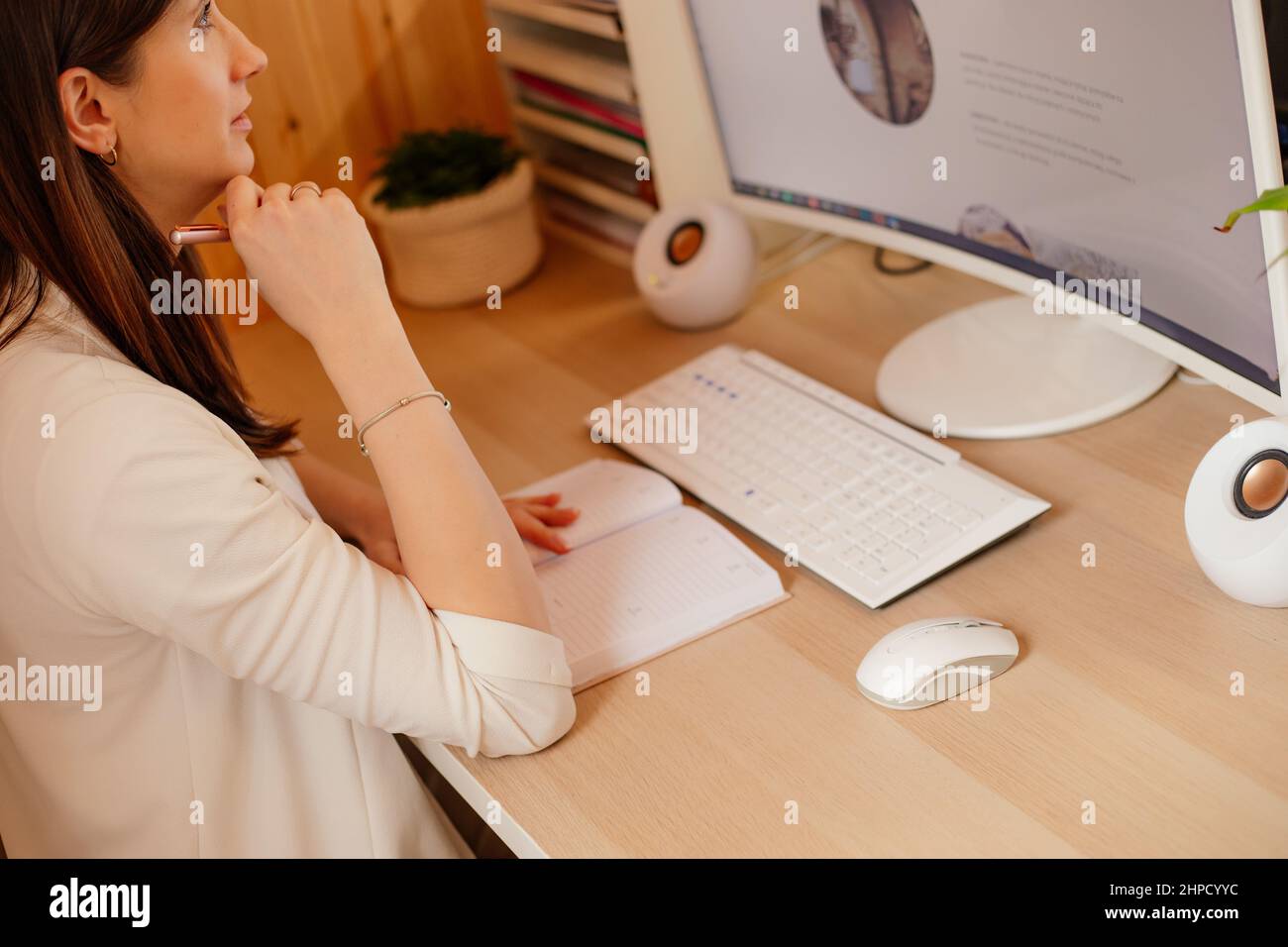 Giovane donna che lavora con lunghi capelli scuri seduti alla scrivania con notebook, tastiera bianca, mouse, altoparlanti a colonna. Foto Stock