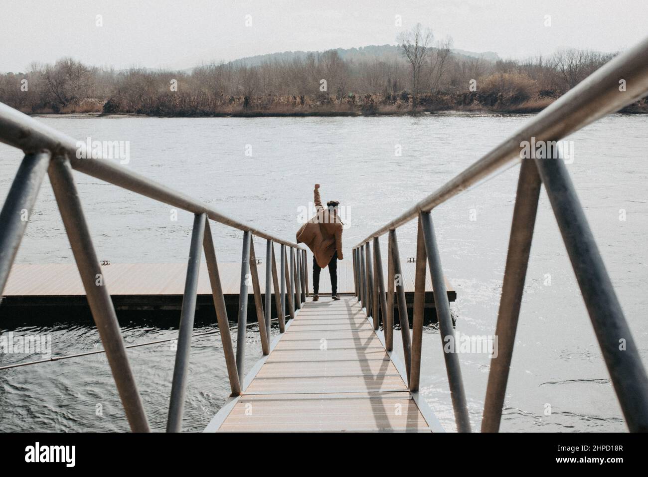 Uomo alla fine di una passerella di legno accanto ad un fiume che alza un braccio in vittoria. Successo e fiducia in se stessi Foto Stock