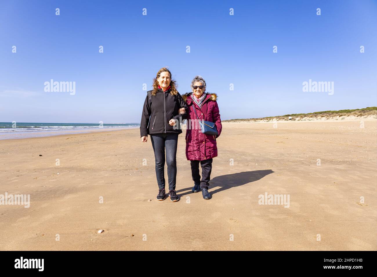 Una donna matura che cammina con la madre anziana in spiaggia in autunno Foto Stock