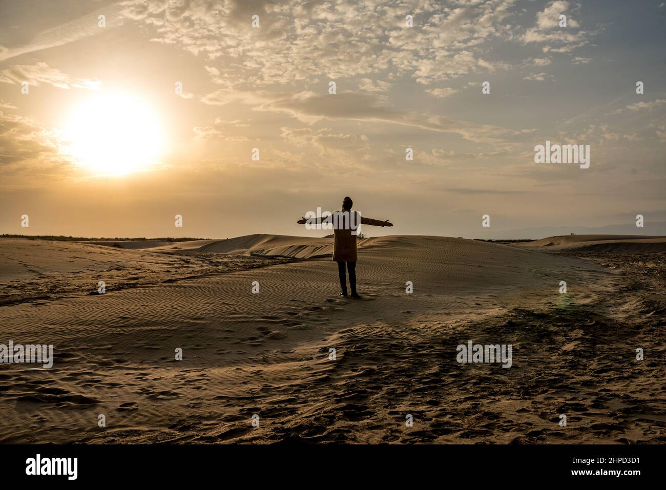 Uomo in piedi sulle dune di una spiaggia al tramonto. Deserto e sabbia. Foto Stock