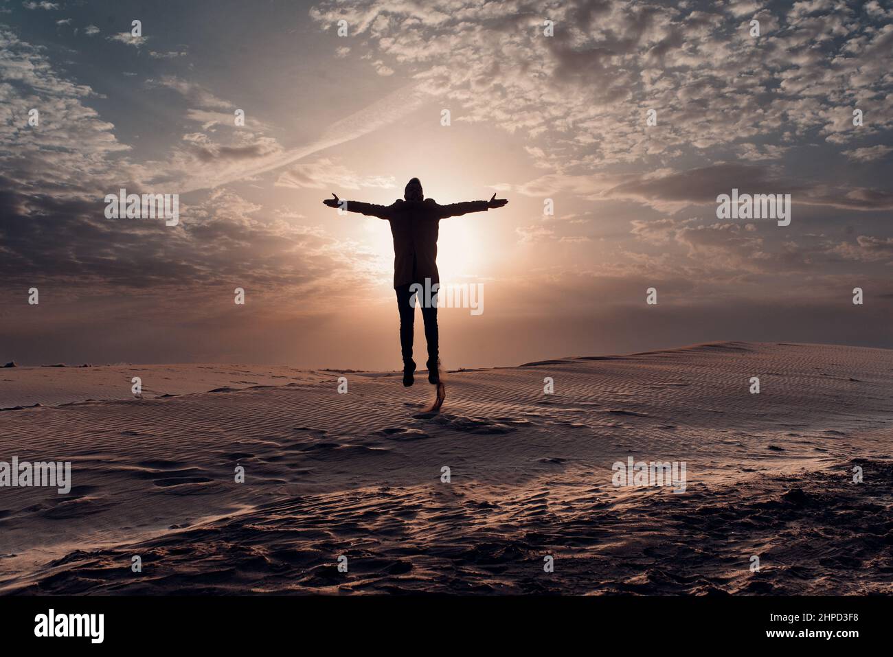 Silhouette di un uomo che salta sulle dune al tramonto. Deserto e sabbia. Foto Stock