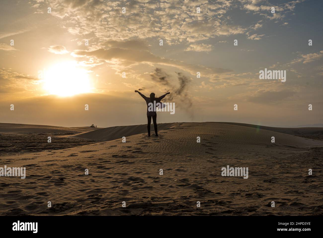 Donna che getta sabbia sulle dune di una spiaggia al tramonto. Libertà Foto Stock