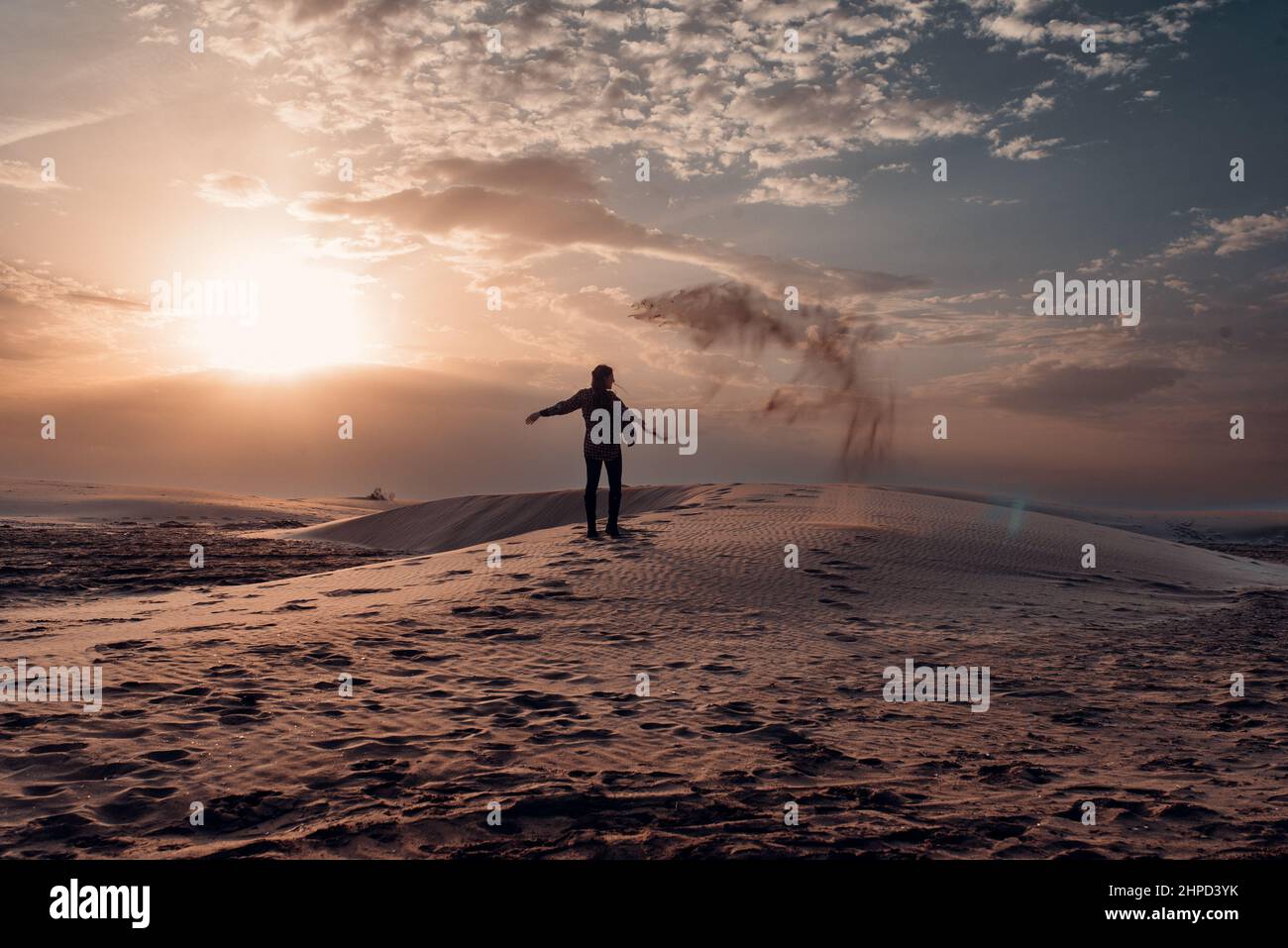 Donna che getta sabbia sulle dune di una spiaggia al tramonto. Foto Stock