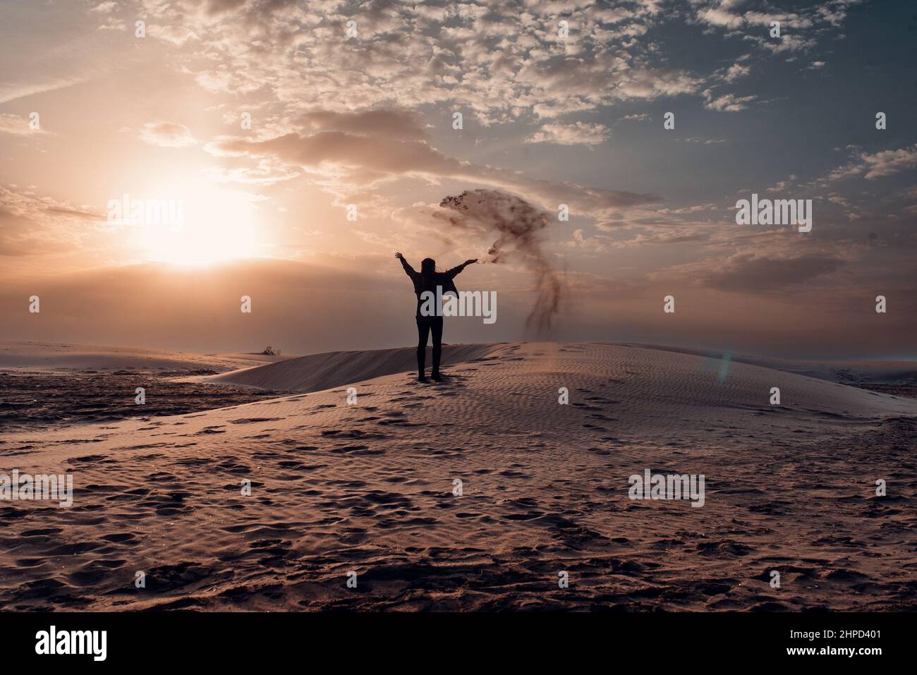 Donna che getta sabbia sulle dune di una spiaggia al tramonto. Foto Stock