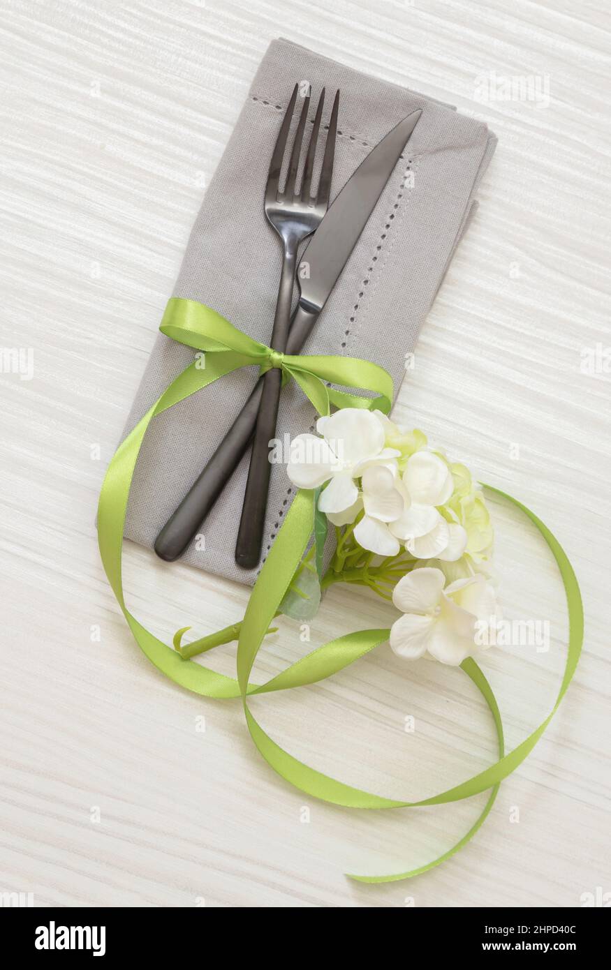 Tavolo per le vacanze di primavera. Eleganti posate, tovagliolo in tessuto grigio e decorazione floreale su legno bianco, Pasqua, menu di nozze, vista dall'alto Foto Stock