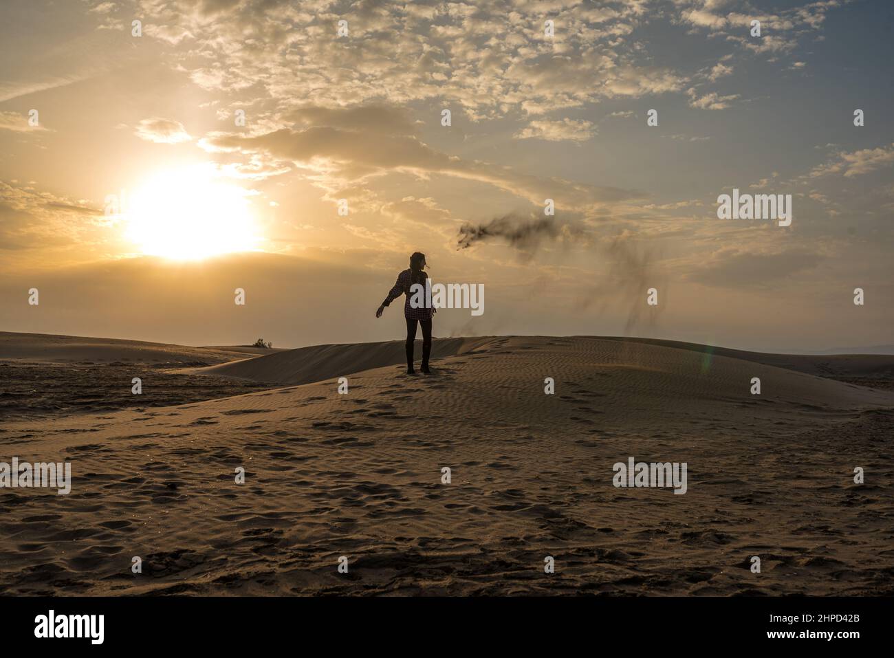 Donna che getta sabbia sulle dune di una spiaggia al tramonto. Foto Stock