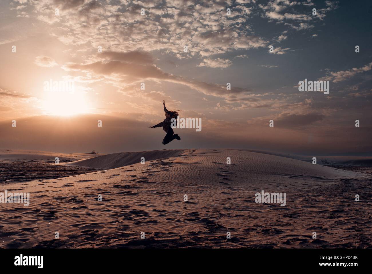 Donna che getta sabbia sulle dune di una spiaggia al tramonto. Libertà Foto Stock