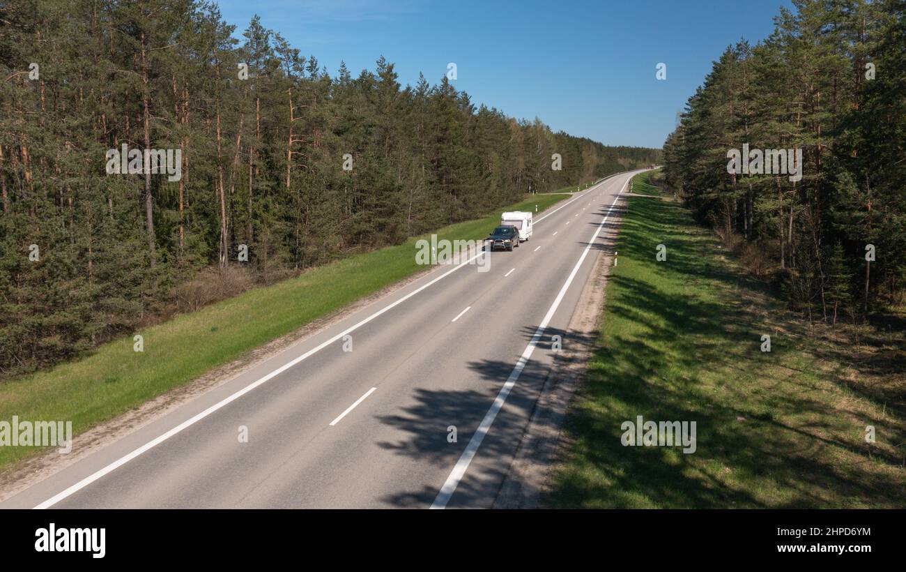 Un'auto solitaria con Camper sta guidando su una strada rurale vuota un concetto di viaggiatore unico Foto Stock
