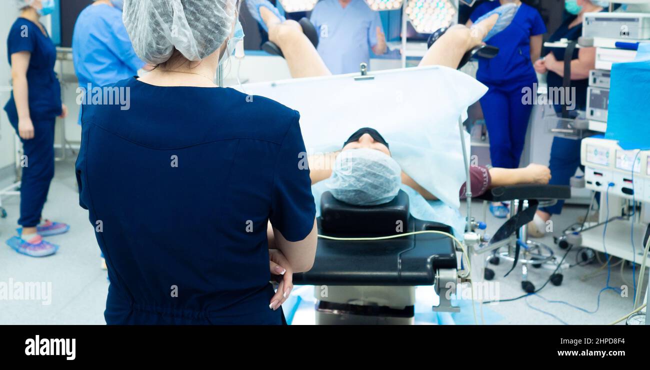 La donna è un medico nella sala operatoria. Vista posteriore. Vista della schiena del medico sullo sfondo del paziente sul tavolo operatorio. Foto Stock