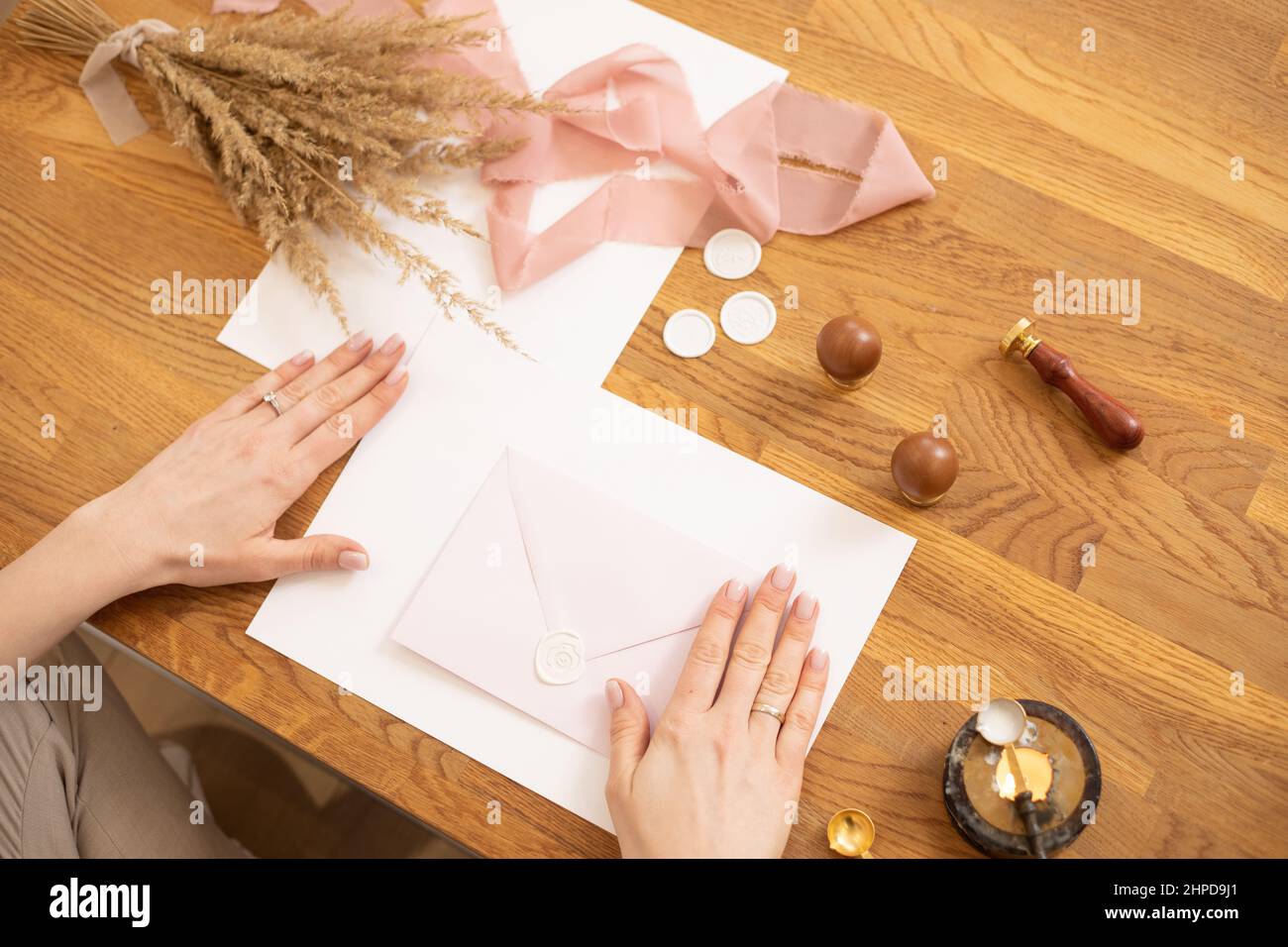 Foto ritagliata di mani donna che fanno sarchiatura invito busta mestiere, decorare con nastro rosa e cera di sigillo. Vista dall'alto Foto Stock