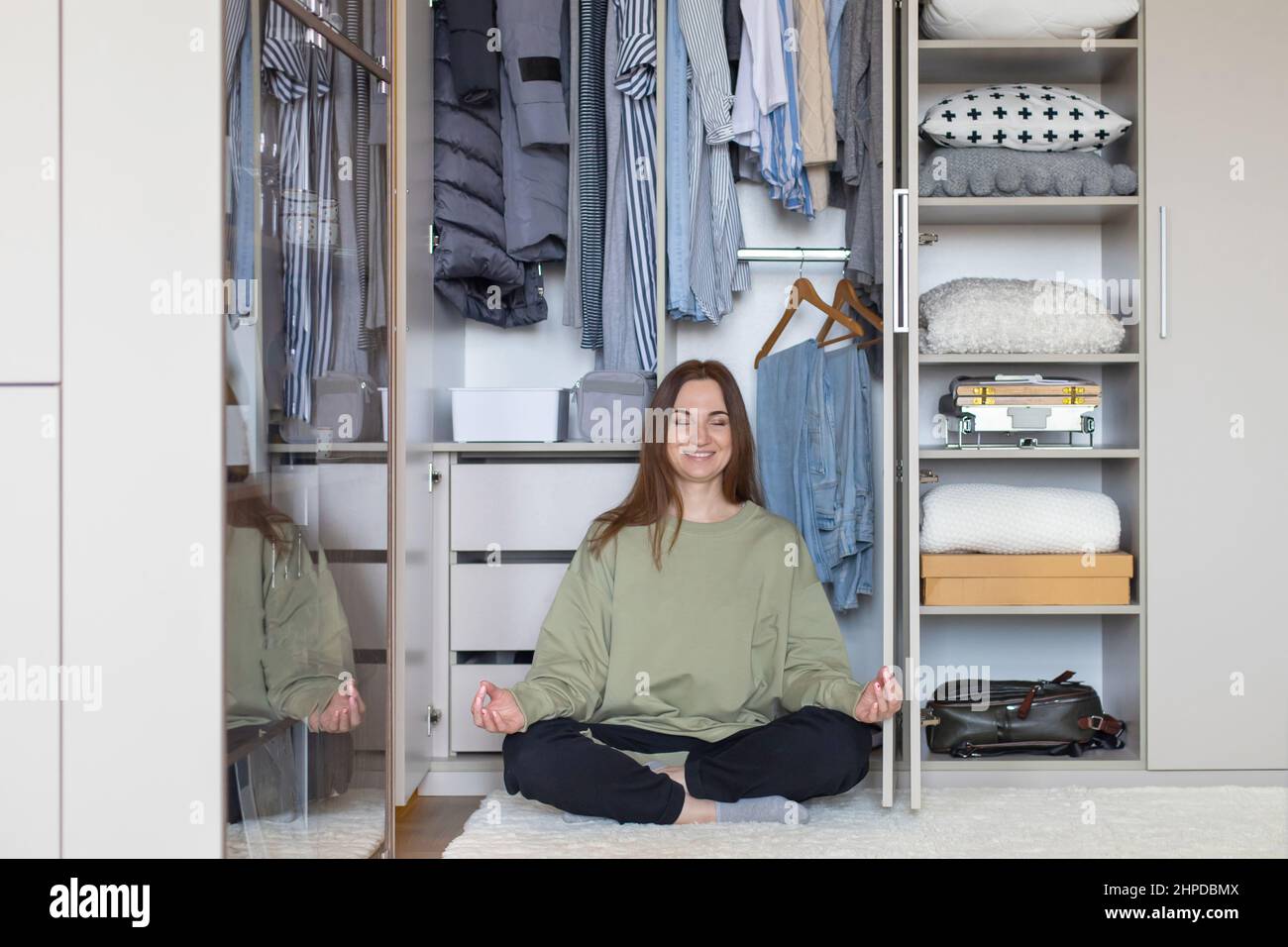 Donna allegra in posizione lotus a moderno armadio di stoccaggio. Felice casalinga che posa meditando Foto Stock