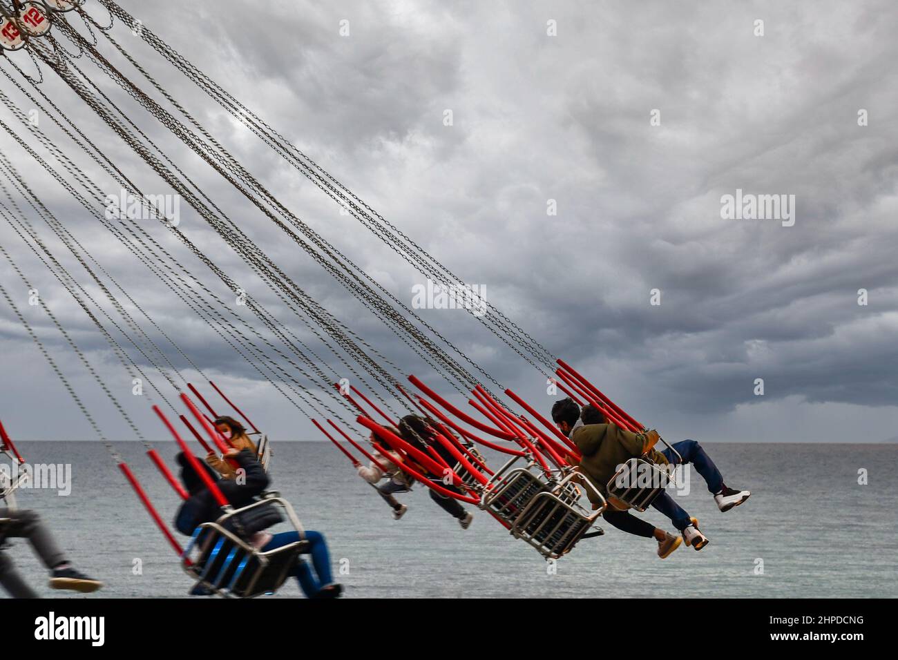 Gli adolescenti si divertono in un giro a catena sulla riva del mare con cielo nuvoloso, Sanremo, Imperia, Liguria, Italia Foto Stock