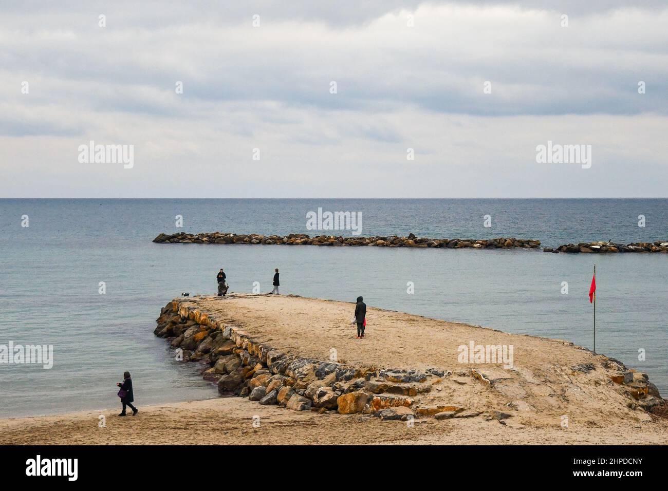 Vista ad alto angolo della spiaggia in inverno con persone in piedi su un frangiflutti rocciosi, Sanremo, Imperia, Liguria, Italia Foto Stock