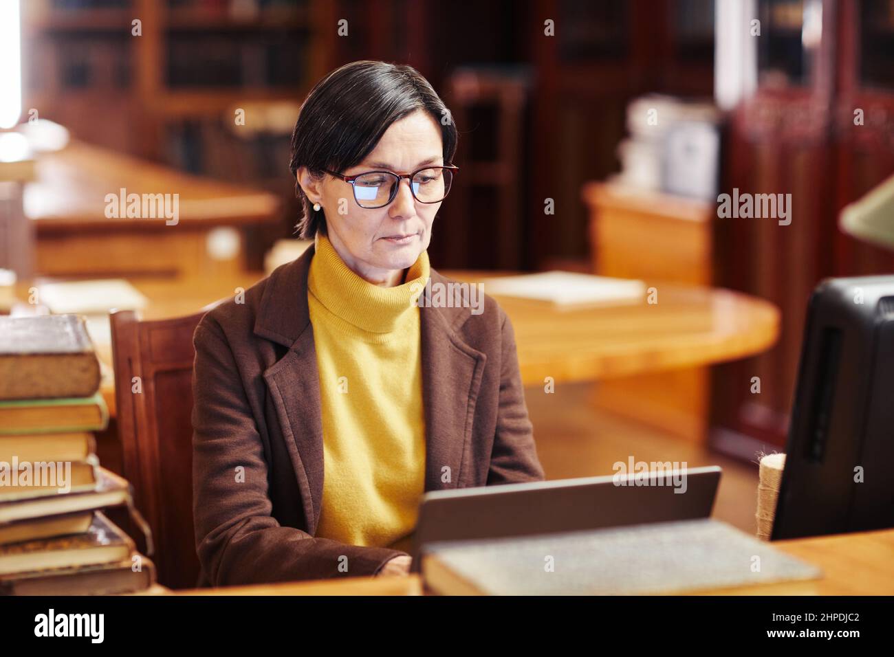 Ritratto di bibliotecaria femminile con un computer portatile mentre si lavora con il catalogo dei libri Foto Stock