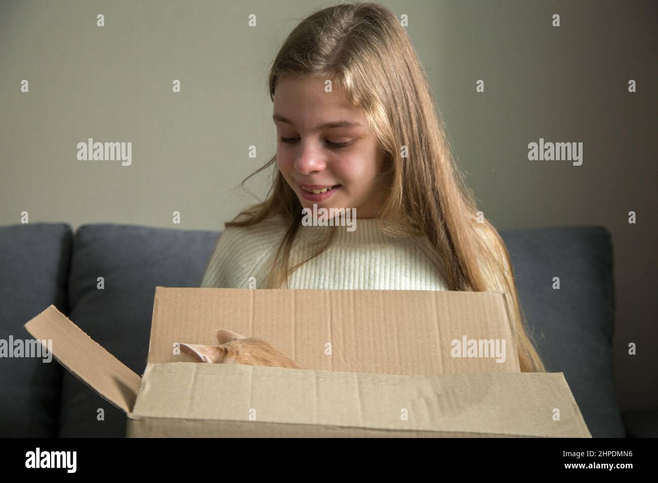 la ragazza felice apre un regalo dove ci è un gattino in una scatola del regalo, un regalo di compleanno Foto Stock