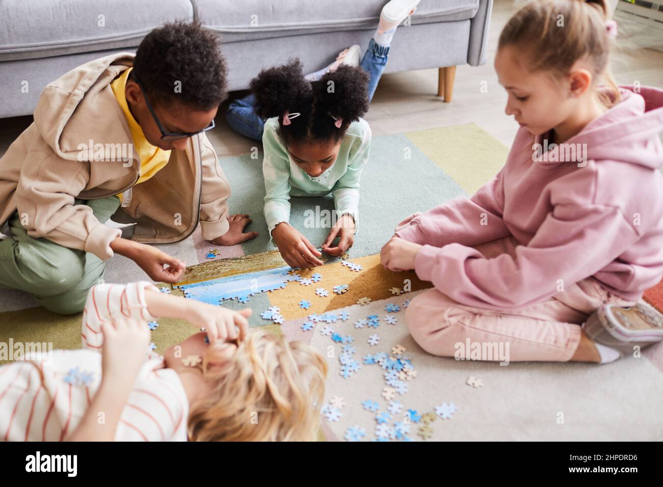 Ritratto ad alto angolo di diversi gruppi di bambini che giocano con gioco di puzzle sul pavimento insieme Foto Stock