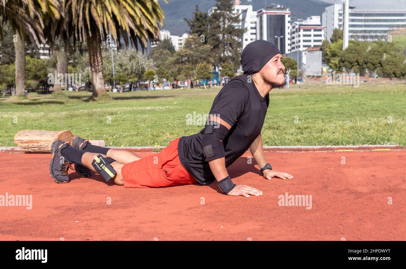 Il giovane latino che fa cobra si allunga durante una routine di esercizio in un parco al mattino Foto Stock