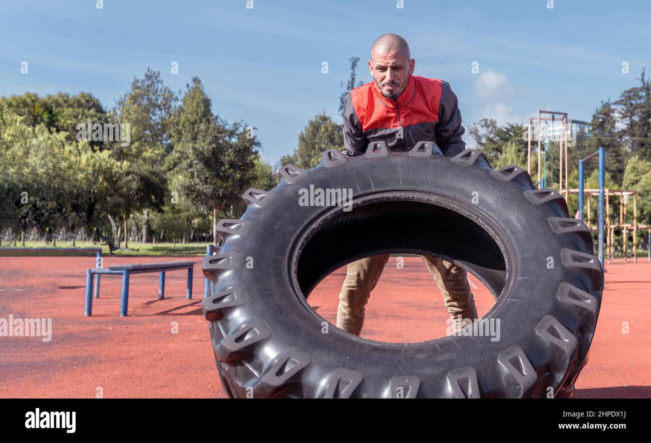 L'uomo che fa la forza sollevando un pneumatico in una procedura di esercitazione per rinforzare i muscoli all'aperto Foto Stock