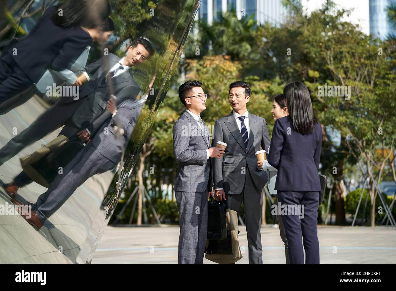 gruppo di quattro giovani uomini d'affari asiatici in piedi chiacchierando all'aperto per strada Foto Stock